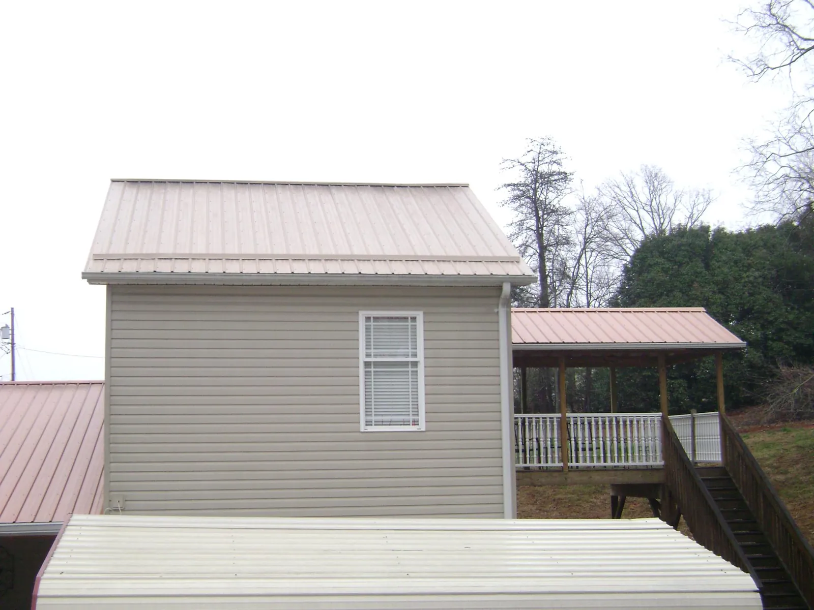 Tan metal roofs on a two story addition and attached porch, from a Roof Replacement job in Newport